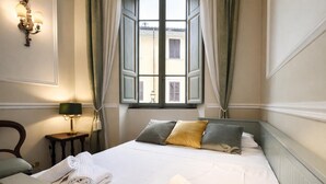 Une chambre d’hôtel avec un lit, une chaise, une lampe et une fenêtre avec des rideaux.