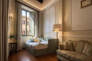 A room with a bed, a sofa, a lamp, and a window with curtains. - Veronica Suite – Historic Center near Piazza Venezia (Roma)