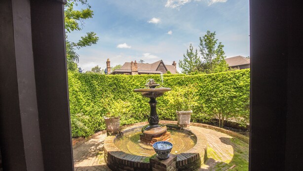 A circular brick fountain with a bowl in the center, surrounded by a brick pathway.