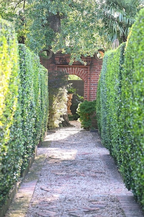 A pathway leading through a garden with a brick archway, surrounded by neatly trimmed hedges.