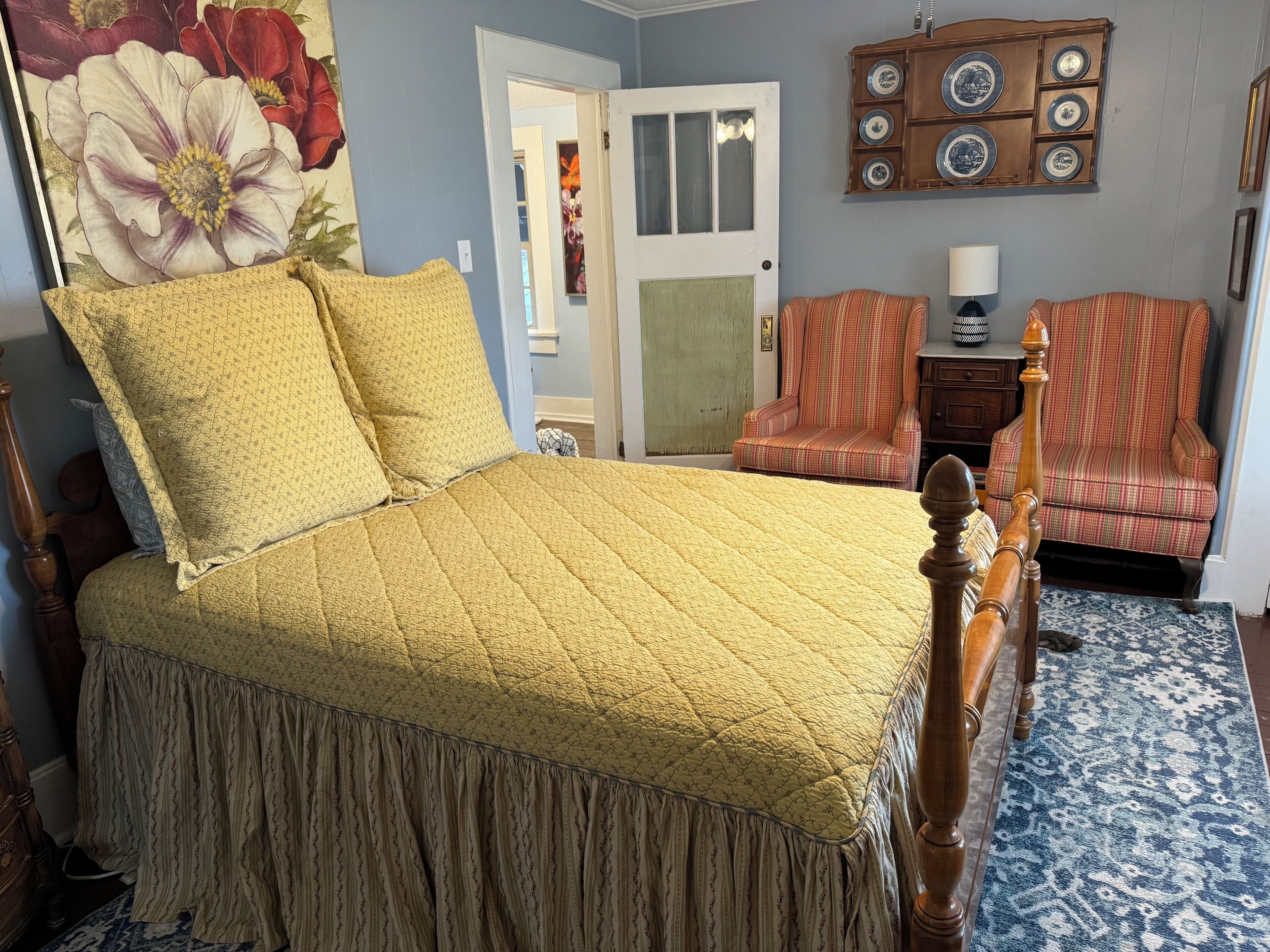 A bedroom with a bed, two chairs, a door, and a wall with a plate display.