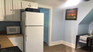 A compact kitchen with a white refrigerator, a microwave, wooden flooring, and a blue door.