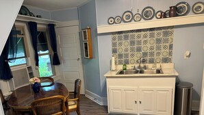 A compact kitchen with a dining area, featuring a tiled backsplash, a sink, and a small trash can.