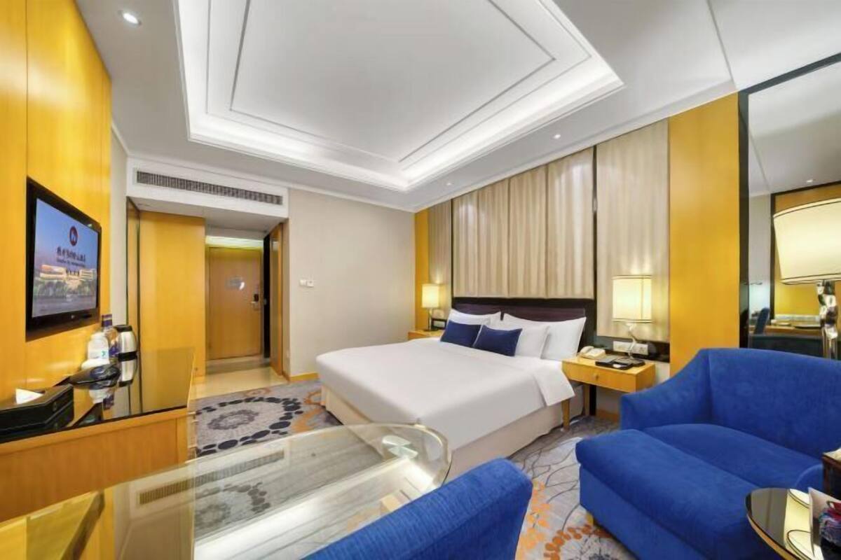 A hotel room with a large bed, a desk with a computer, a TV mounted on the wall, and a blue sofa.