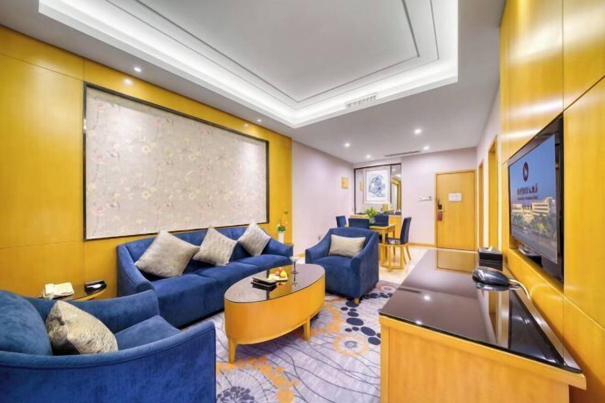 A modern hotel room with a sofa set, a coffee table, a TV, and a large abstract painting on the wall.