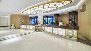 Eine moderne Hotellobby mit einer gebogenen Rezeption, einer zentralen Säule und einer dekorativen Deckenleuchte.