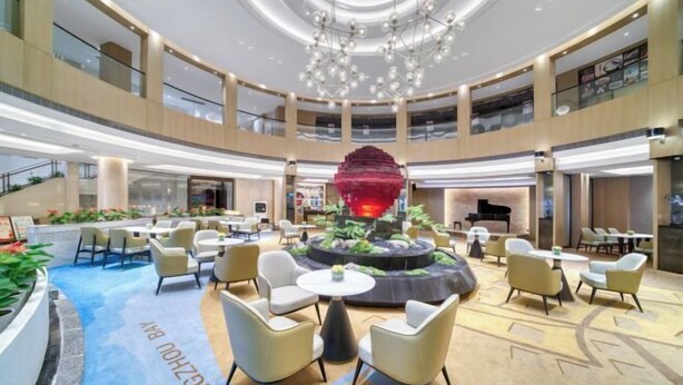 Eine großzügige Lobby mit einer zentralen Wasserspiele-Anlage, mehreren Sitzbereichen und einem modernen Kronleuchter.