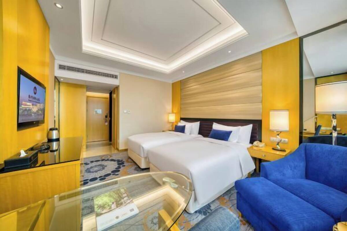 A hotel room with a large bed, a blue sofa, a glass coffee table, and a television on the wall.
