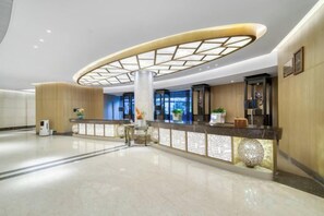 Un hall d’hôtel comprenant un comptoir d’accueil, une grande colonne et un design moderne au plafond.