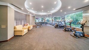 Ein Fitnessraum mit Trainingsgeräten, einer Couch und einem großen Fenster mit Blick auf Grünflächen.
