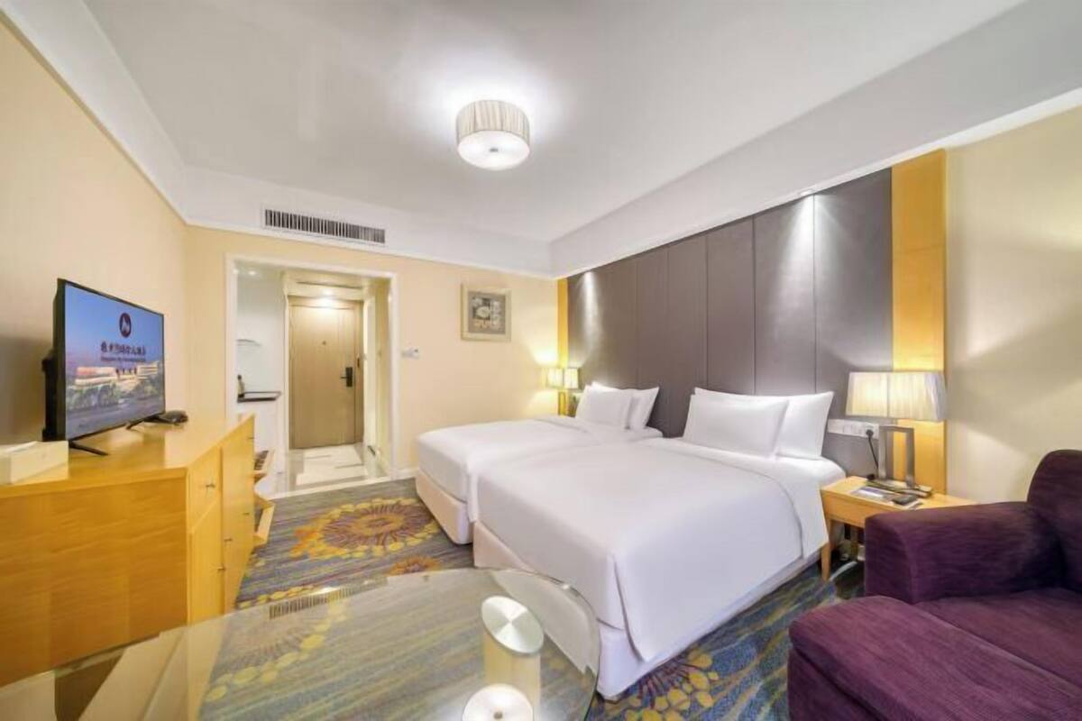 A hotel room with two beds, a desk with a television, a sofa, and a patterned carpet.