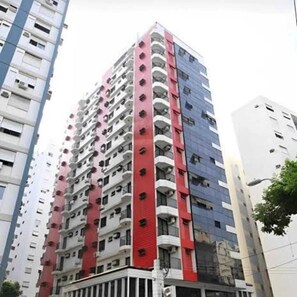 A multi-story building with balconies, a flat facade, and a corner entrance. - Atlântico Flat Gonzaga (Santos)