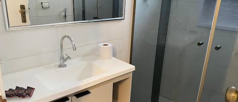Un baño con lavamanos blanco, espejo y cabina de ducha.