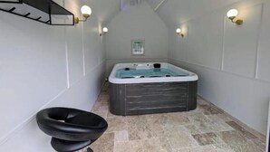 A narrow room with a hot tub, a chair, and wall-mounted lights.