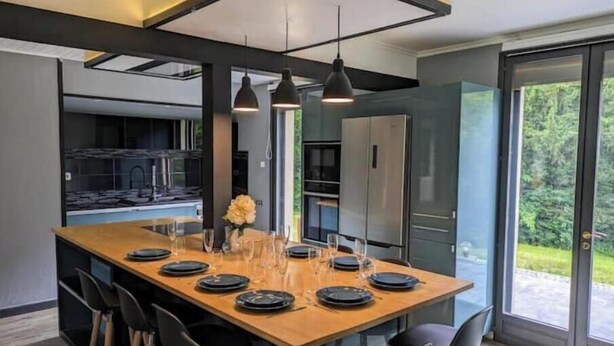 A modern kitchen with a large island, black chairs, and pendant lighting.