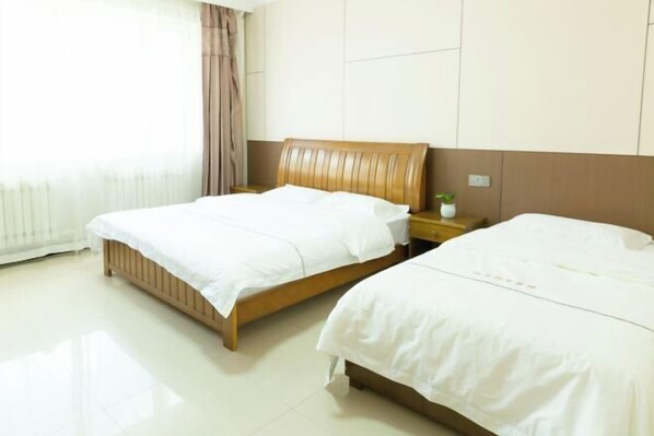 A hotel room with two beds, a wooden headboard, a bedside table with a plant, and a window with curtains.