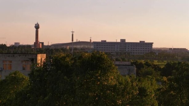 Un edificio con una torre, rodeado de árboles y otras construcciones.