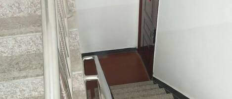 Una escalera alfombrada con barandilla de metal y una puerta de madera al final.