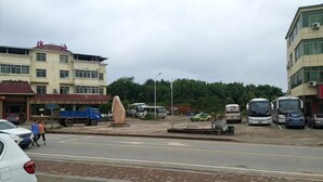 A parking area with multiple vehicles, including cars and buses, and a building with a sign.