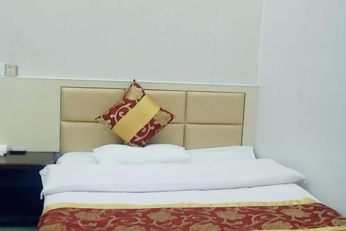 Una habitación de hotel con una cama, cabecera y mesita de noche.
