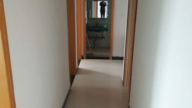 A narrow hallway with wooden doors on either side, leading to a room with a visible sink and mirror.