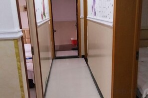 Un pasillo estrecho con una puerta al final, un cubo rojo y una pared blanca con un cartel.
