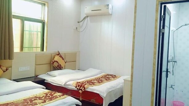 Habitació d'hotel amb dos llits, una finestra amb cortines, aire condicionat i zona de dutxa.