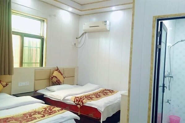 Habitación de hotel con dos camas, una ventana con cortinas, un equipo de aire acondicionado y zona de ducha.