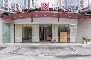 Entrada de hotel con fachada de vidrio, toldo rojo y un letrero sobre la entrada.