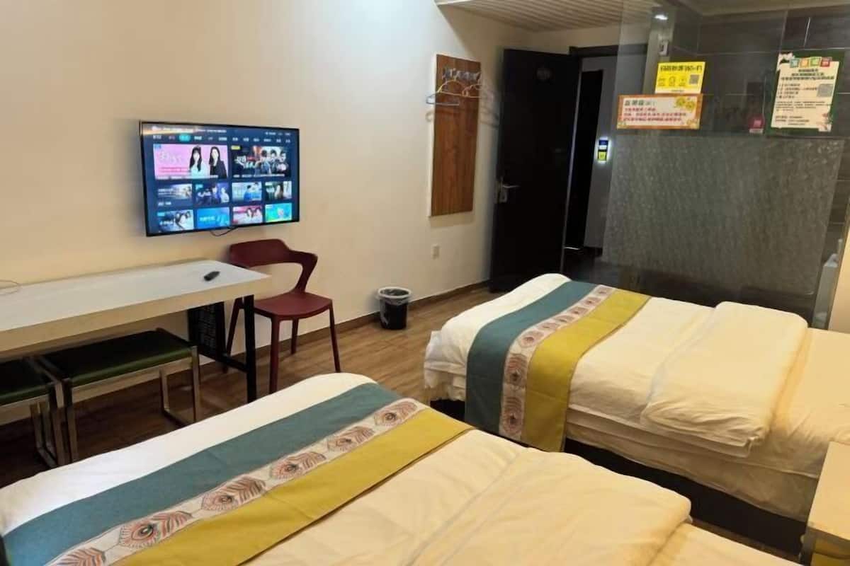 Ein Hotelzimmer mit Schreibtisch, zwei Betten, einem Fernseher, der einen Film zeigt, und einer Tür mit einem Schild.