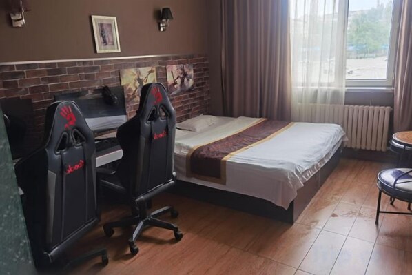 A hotel room with a bed, a desk with two gaming chairs, a window with curtains, and a radiator. - Harbin Cashbox Express Hotel (Harbin)