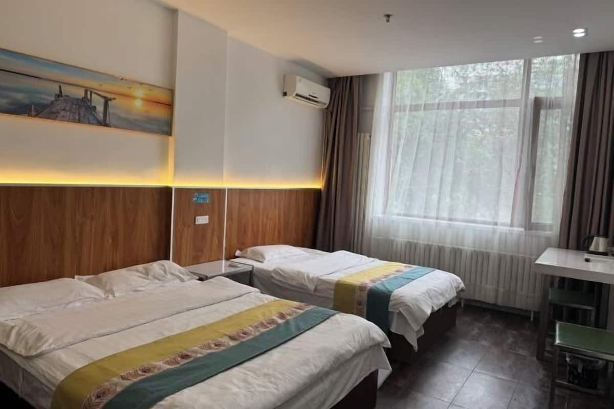 Ein Hotelzimmer mit zwei Betten, einem Fenster mit Vorhängen, einer Klimaanlage und einem Bild an der Wand.