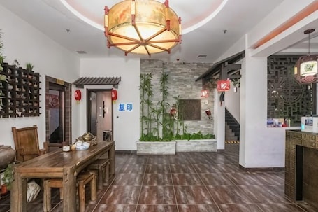 A traditional-style interior with a wooden dining table, a large hanging light fixture, and a stone wall with vertical plants.. Harbin Cashbox Express Hotel