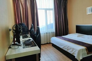 A hotel room with a bed, a desk with a computer, and a window with curtains.