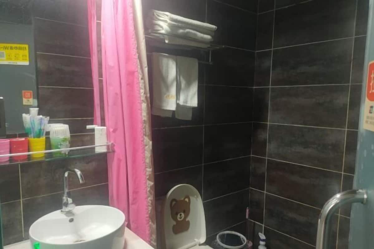 Ein Badezimmer mit Waschbecken, Toilette mit Teddybär-Dekoration, Ablagefläche für Pflegeprodukte und einem rosa Vorhang.