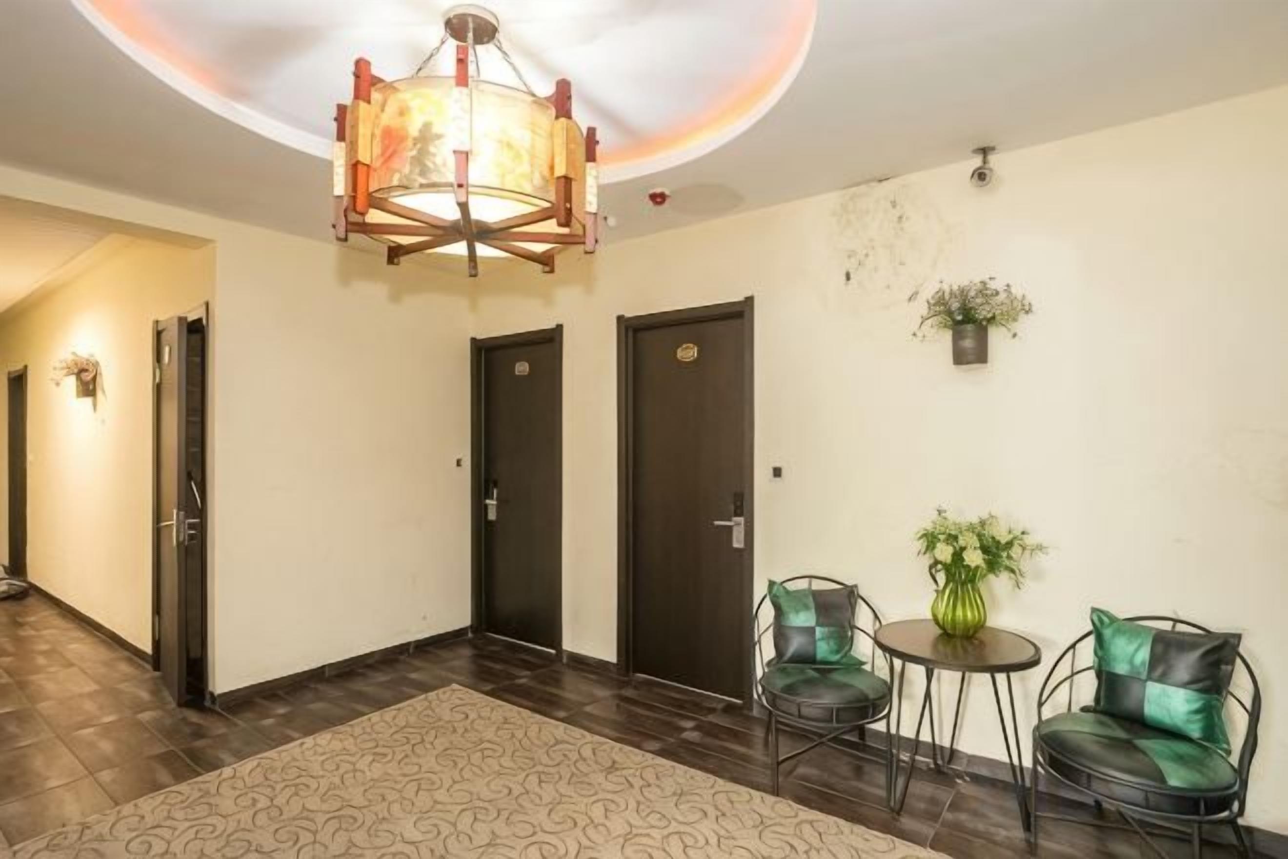 A hotel lobby with a chandelier, two doors, a small table with a plant, and two chairs.