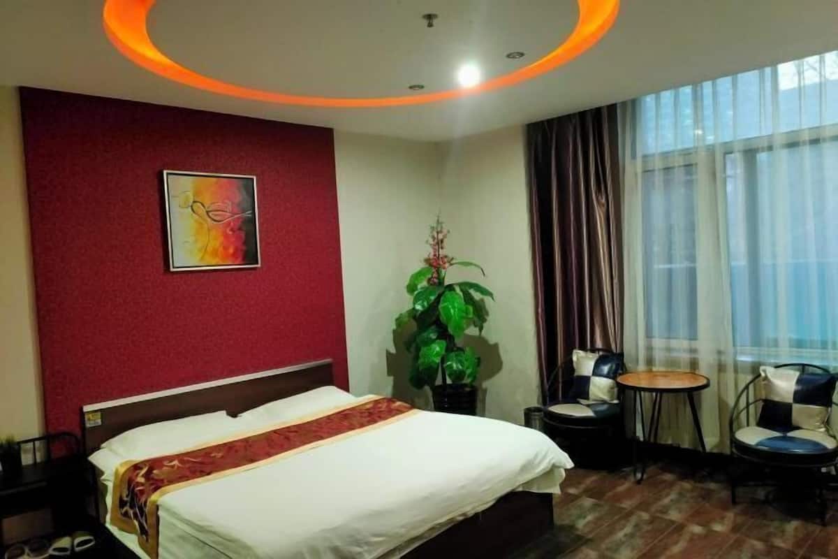 Ein Hotelzimmer mit einem Bett, einem kleinen Tisch, zwei Stühlen, einer Topfpflanze und einem fenster mit Vorhängen.