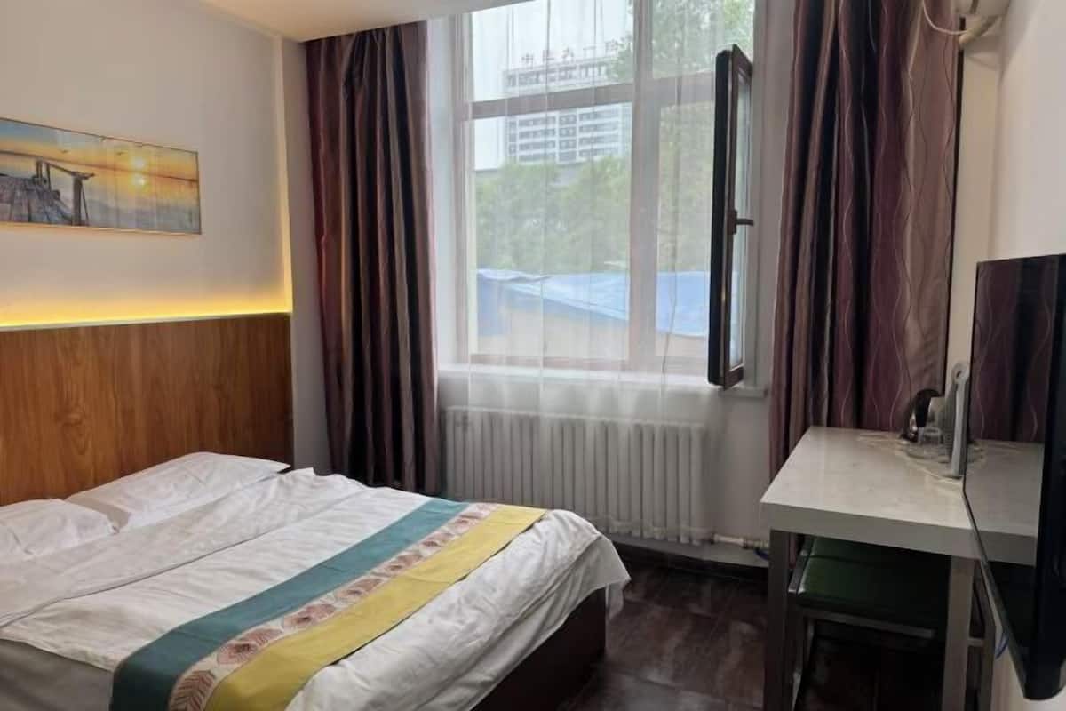 Ein Hotelzimmer mit Bett, Schreibtisch, Fenster mit Vorhängen, Heizkörper und einem Bild an der Wand.