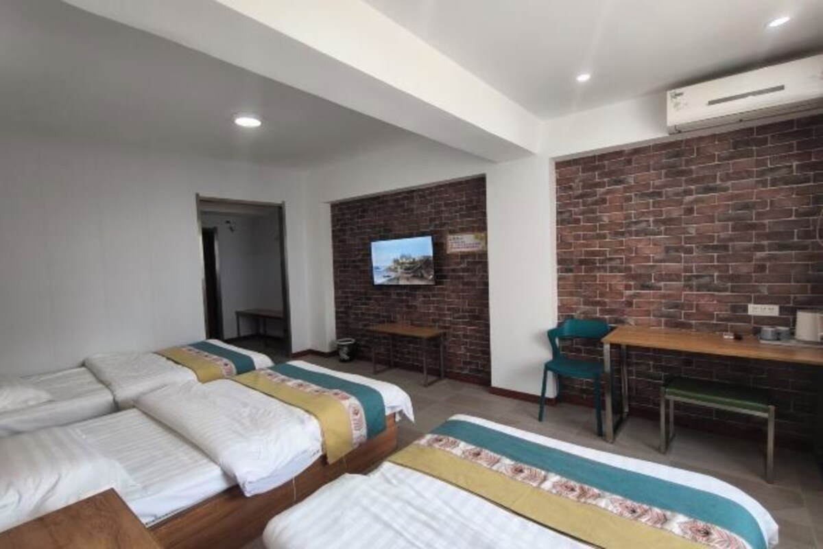 Habitación de hotel con dos camas individuales, un escritorio, una silla y un televisor montado sobre una pared de ladrillo.