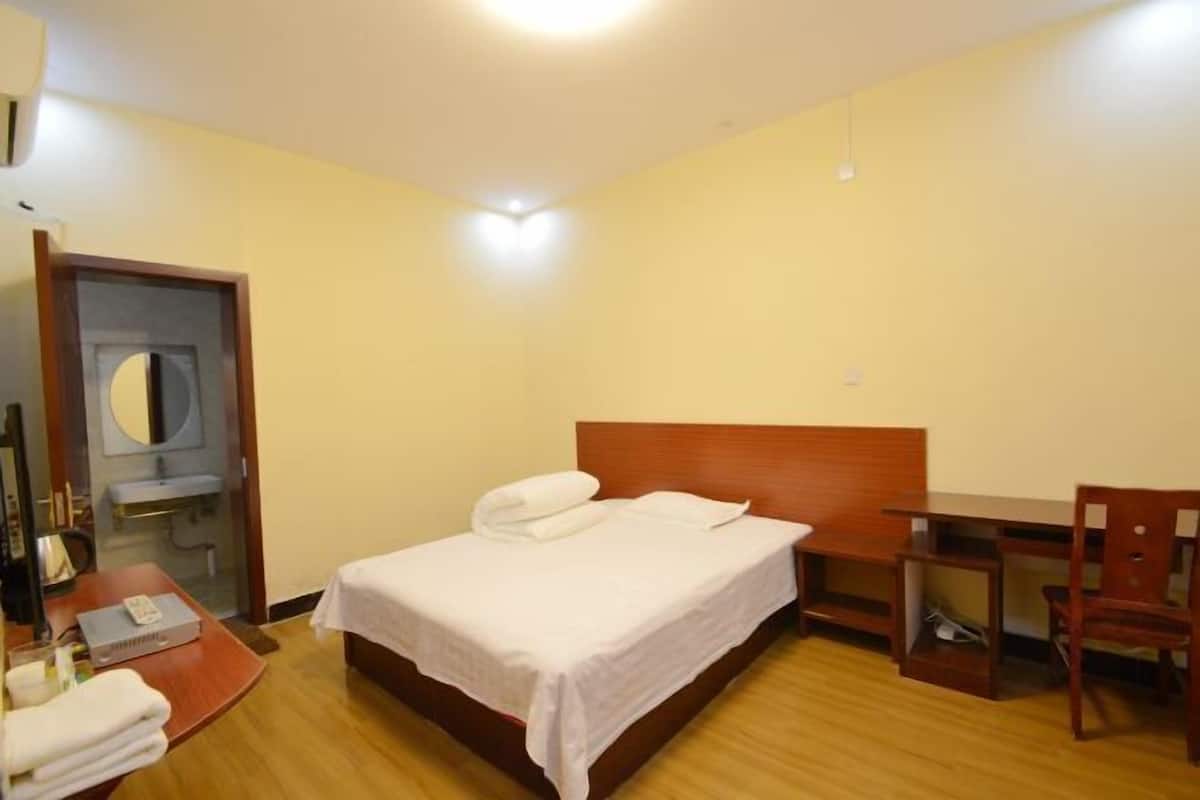 A hotel room with a bed, a desk, a chair, a mirror, and a bathroom visible through an open door.