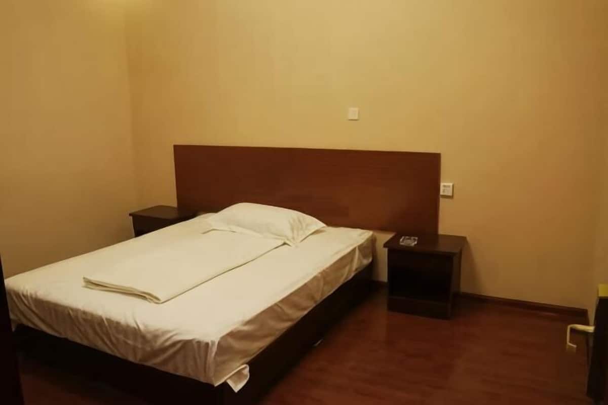 A single bed with a wooden headboard, a bedside table with a lamp, and a wall socket.