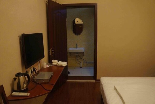 A hotel room with a bed, a desk with a laptop, a television, a kettle, and a bathroom visible through an open door. - Yinxinglou Hotel (Dingyuan)