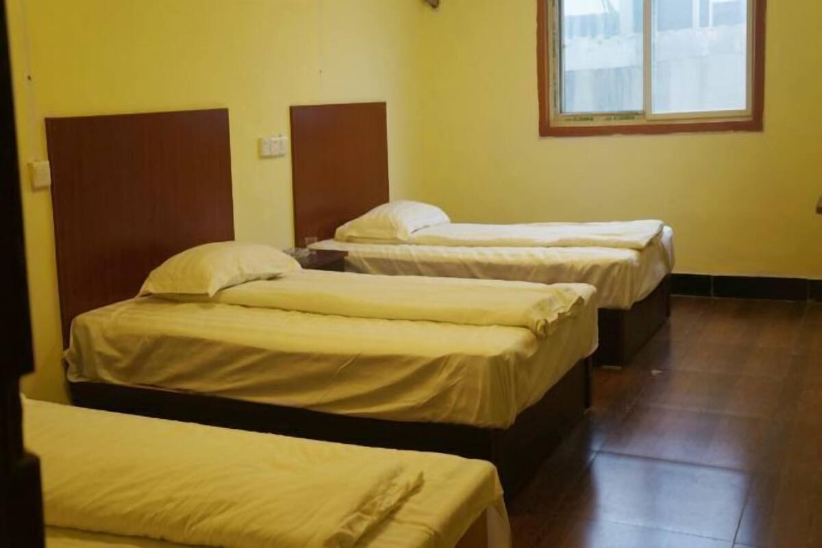 A room with three single beds, wooden headboards, and a window with a view.