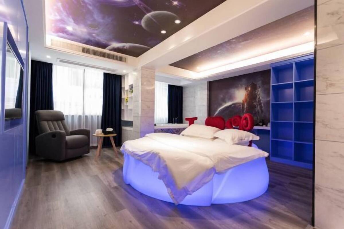 A modern bedroom with a curved bed, a reclining chair, and a wall mural.