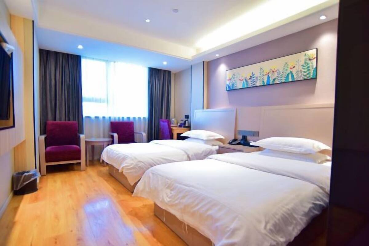 A hotel room with two beds, a chair, a small table, and a painting on the wall.