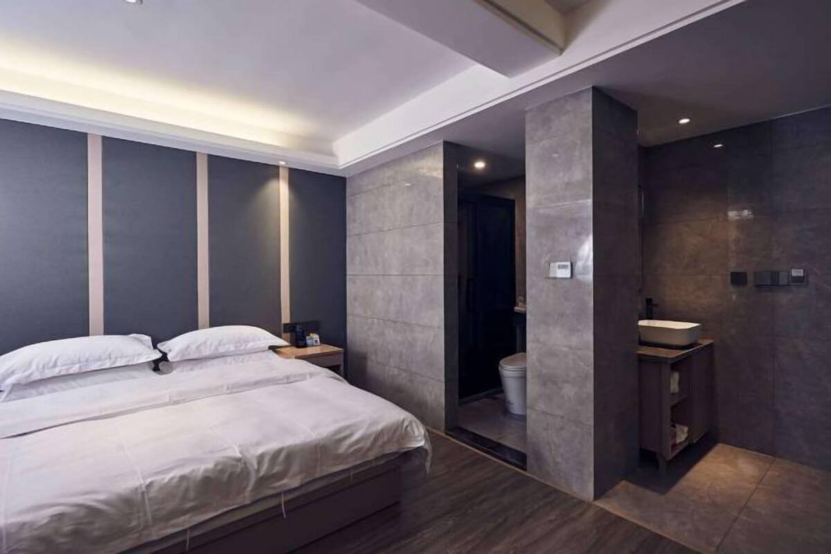 A modern bedroom with a bed, bedside table, and a bathroom with a sink and toilet.
