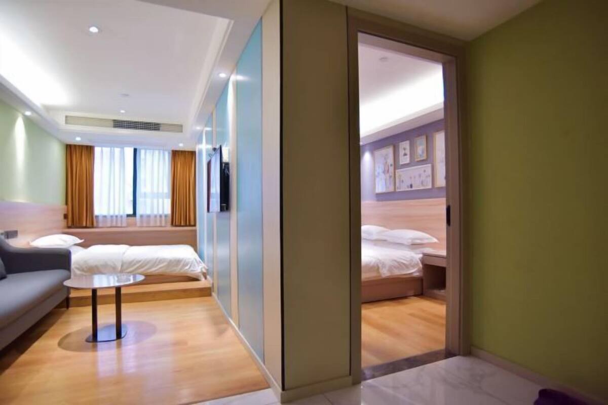 A modern hotel room with a sofa, a small table, a bed, and a bathroom visible through a door.