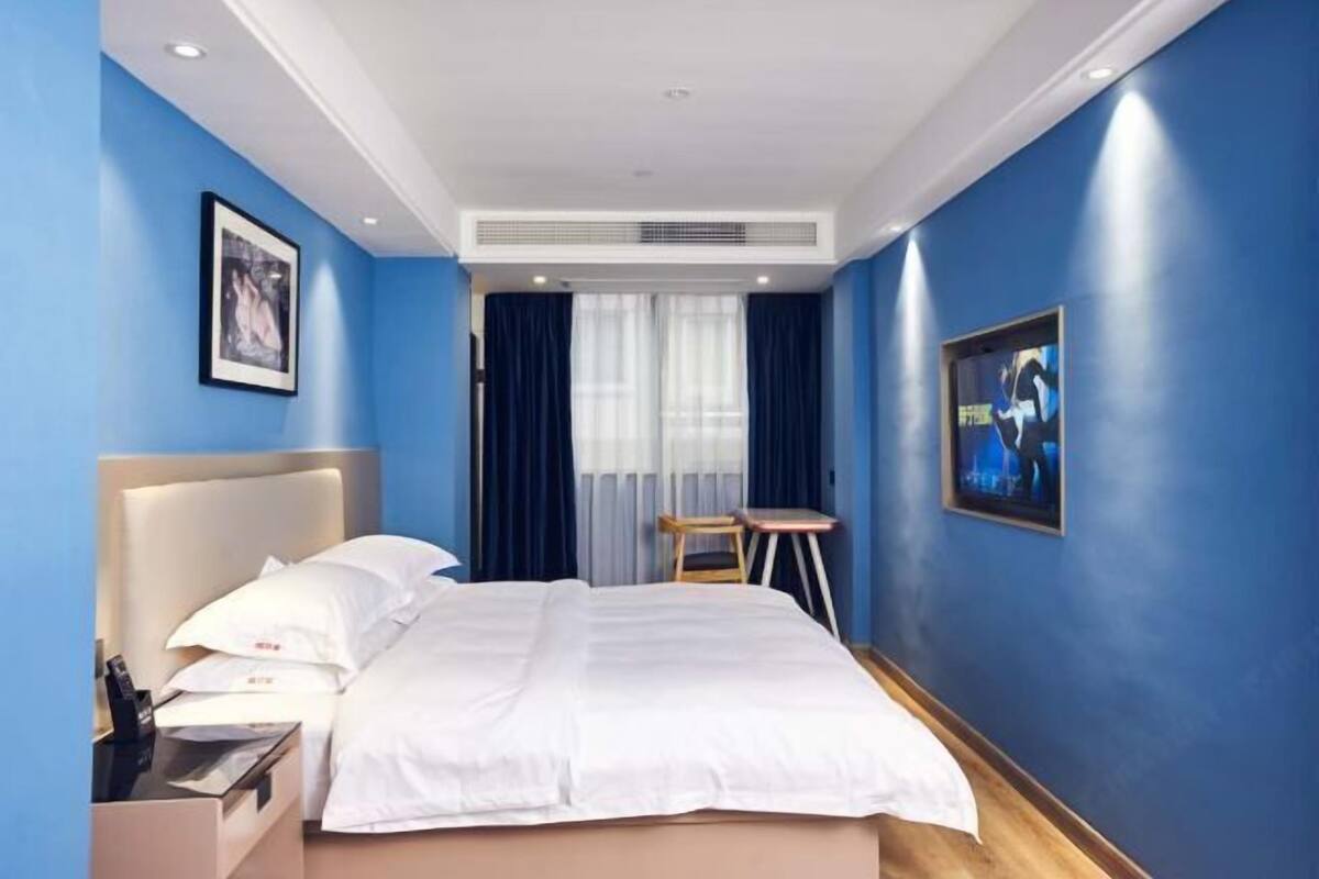 A hotel room with a bed, bedside table, and a window with curtains.
