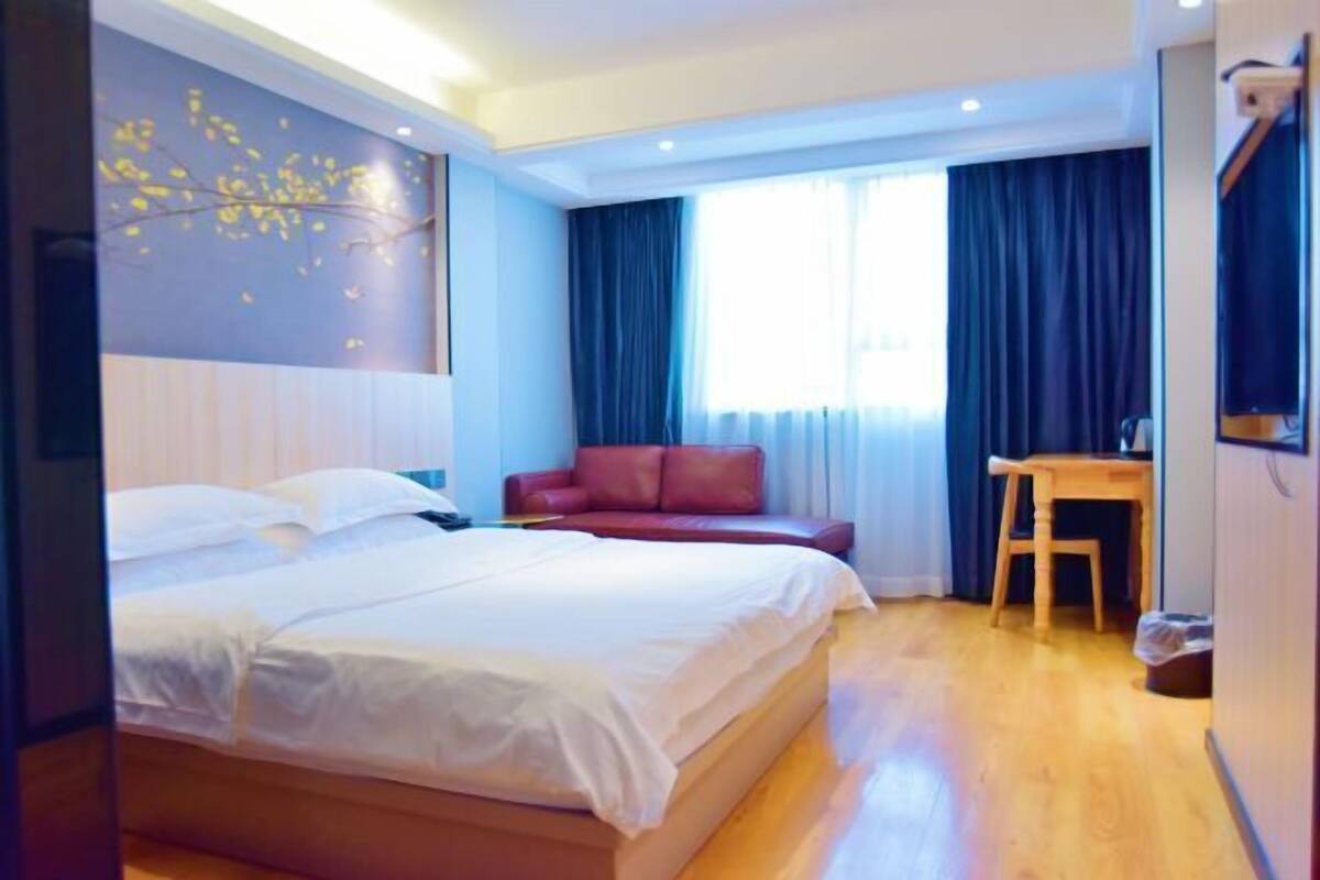 A hotel room with a bed, a red sofa, a wooden table, and a window with curtains.