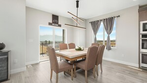 Un comedor moderno con una mesa de madera y sillas acolchadas, una lámpara de techo y vistas al exterior a través de un ventanal.